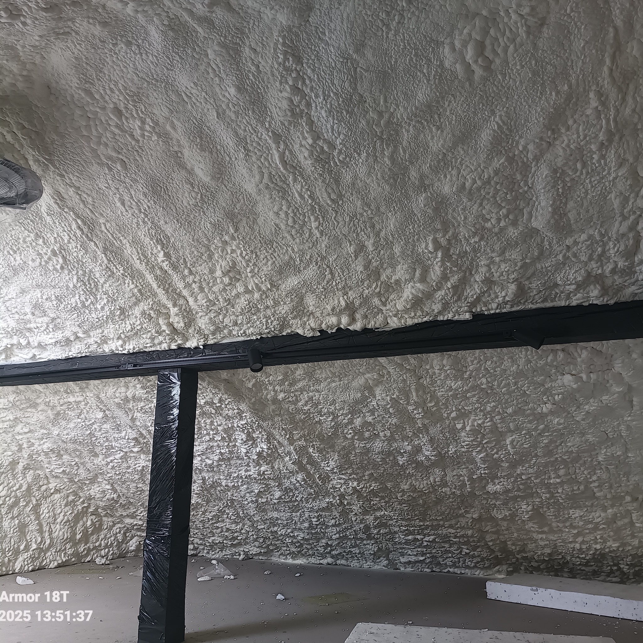 Poddasze po ociepleniu pianką PUR, widoczne czarne elementy konstrukcyjne. Pianka ma nieregularną strukturę, pokrywa całą powierzchnię.