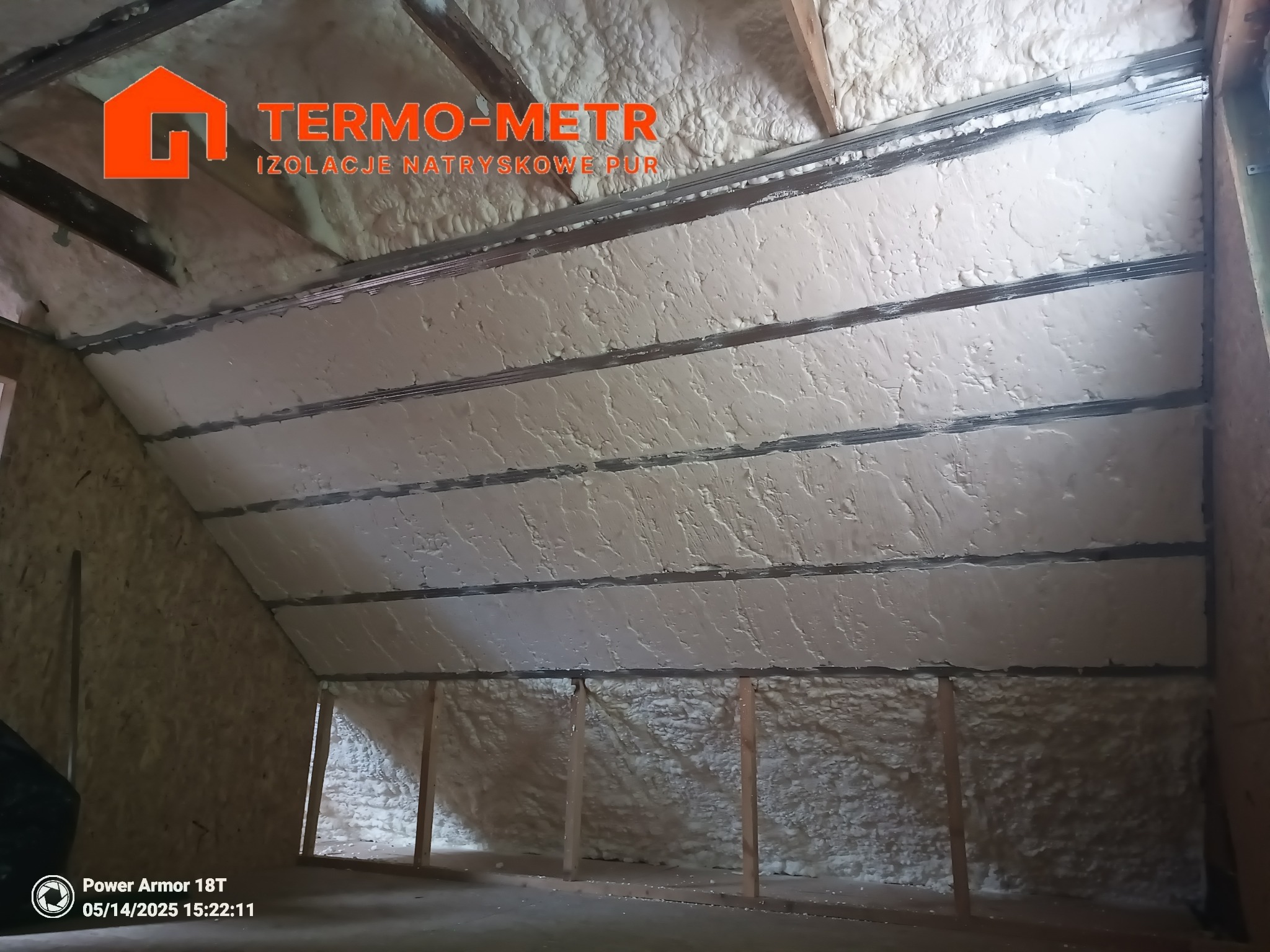 Poddasze z widoczną warstwą izolacji natryskowej PUR między krokwiami, wykonaną w jasnym odcieniu, z widocznymi metalowymi profilami.