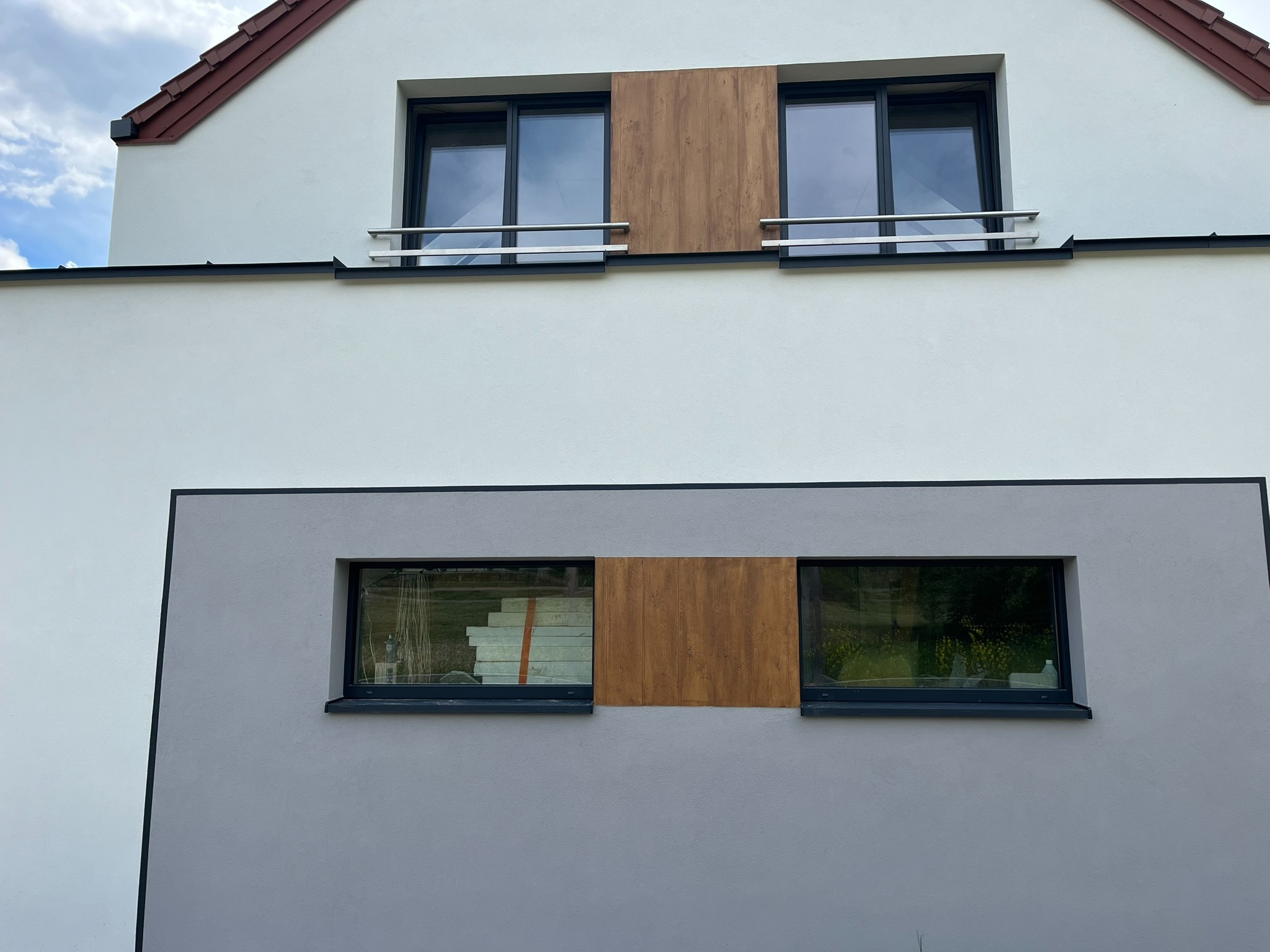 Elewacja budynku po remoncie z oknami, częściowo zasłoniętymi płytami imitującymi drewno; w jednym oknie widoczne płyty ociepleniowe.