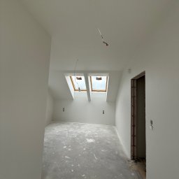 TDM House - Wnętrze poddasza po remoncie, świeżo pomalowane na biało, z dwoma oknami dachowymi i widocznymi gniazdkami elektrycznymi. Podłoga zabezpieczona folią malarską.
