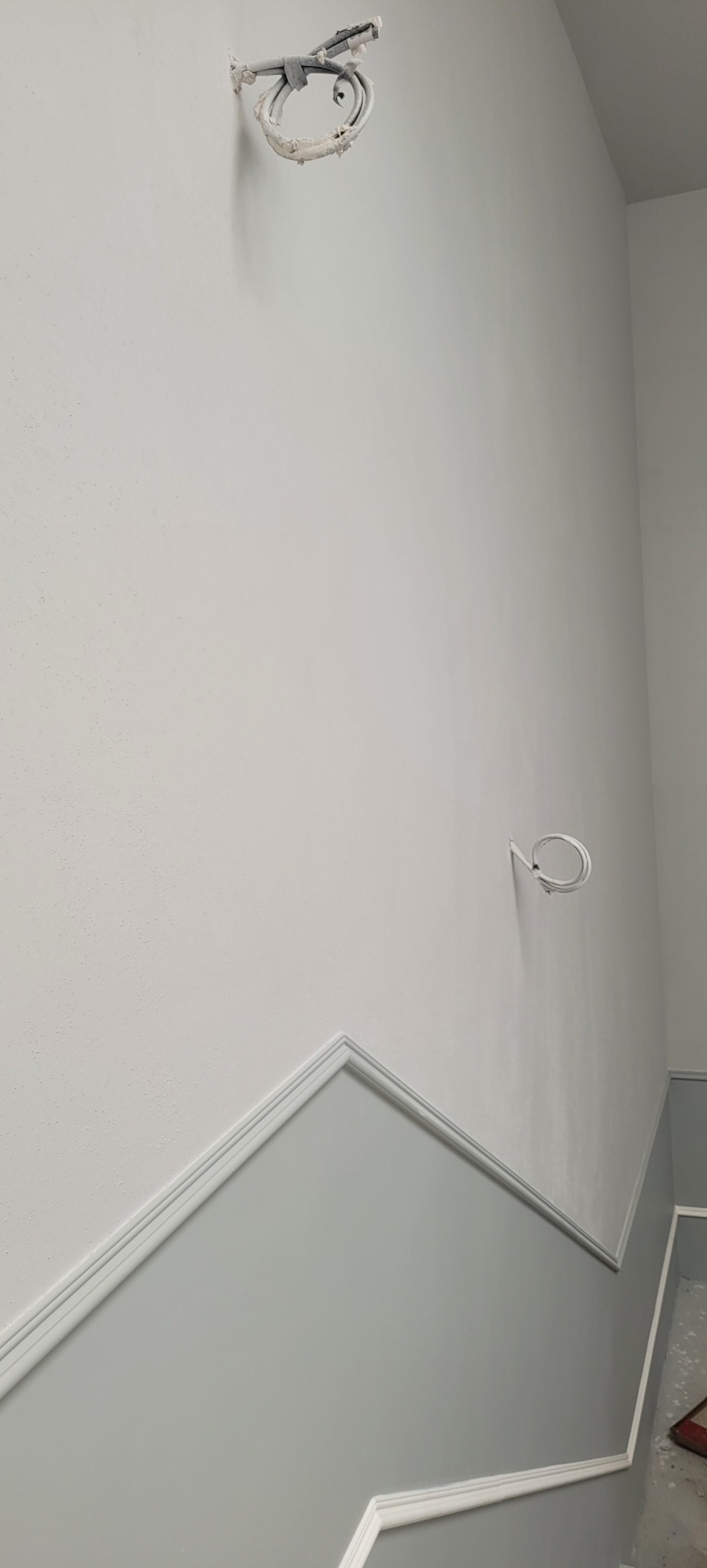 Świeżo pomalowana ściana w pomieszczeniu, z dekoracyjną listwą oddzielającą szary dół od białej góry, widoczne wystające kable w dwóch miejscach.