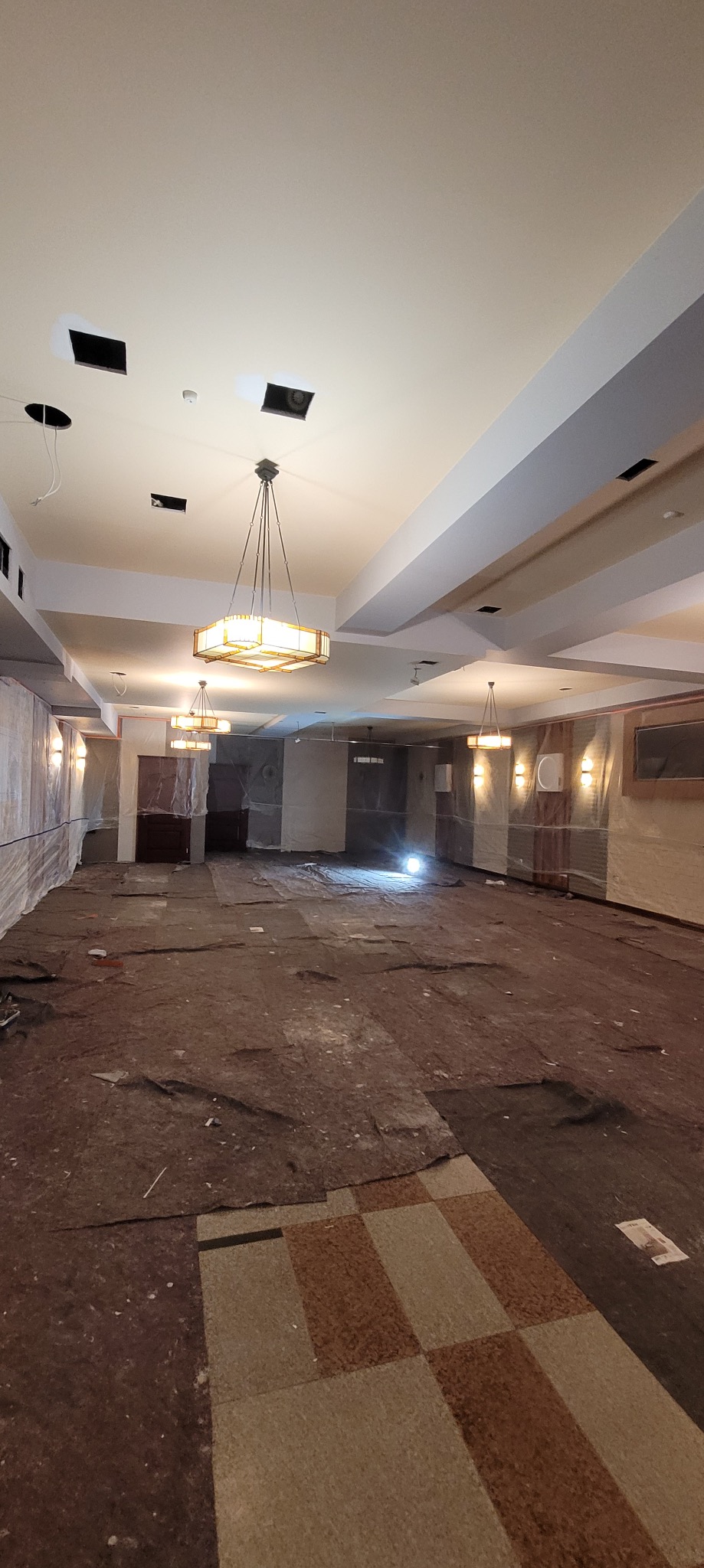 Przygotowanie do prac wykończeniowych we Wrocławiu: zabezpieczone ściany folią, widoczne lampy i fragment starej podłogi przed dalszymi etapami remontu.