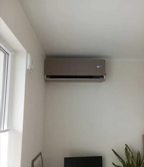 Beżowy klimatyzator ścienny z wyświetlaczem temperatury '30' zamontowany w jasnym pokoju obok okna.