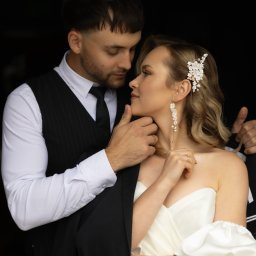 Piotr Krukowski - Elegancka para młoda w zbliżeniu, panna młoda z kwiatowym akcentem we włosach i delikatnymi kolczykami, pan młody w klasycznym garniturze, romantyczne spojrzenie.