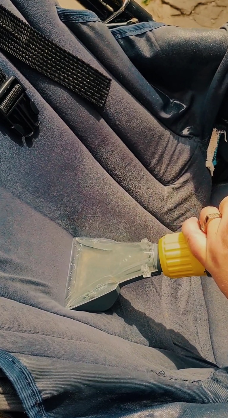 Czyszczenie wózka dziecięcego za pomocą odkurzacza piorącego z żółtą końcówką. Widoczna struktura materiału i elementy mocujące wózka.