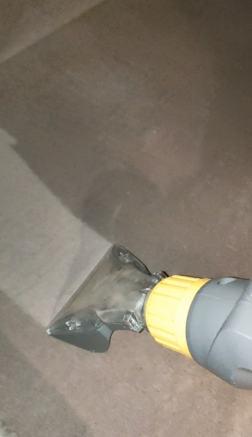 Dysza odkurzacza piorącego w trakcie czyszczenia jasnobrązowej, tekstylnej powierzchni. Widoczny efekt odsysania wody.