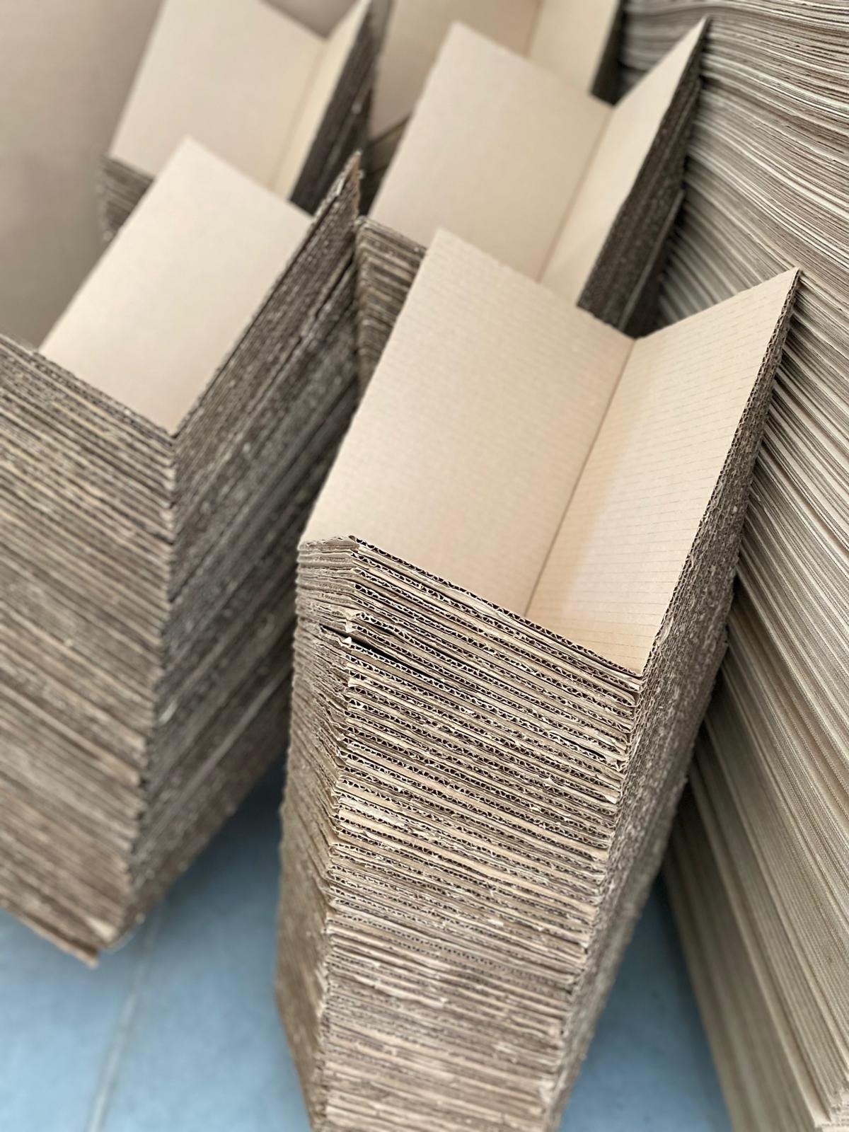 Stosy rozłożonych, tekturowych narożników ochronnych w magazynie, widoczne warstwy tektury falistej.