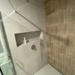 Nowoczesna kabina prysznicowa z wnęką na kosmetyki, wykończona płytkami w dwóch odcieniach, prezentowana w Dziemianach.