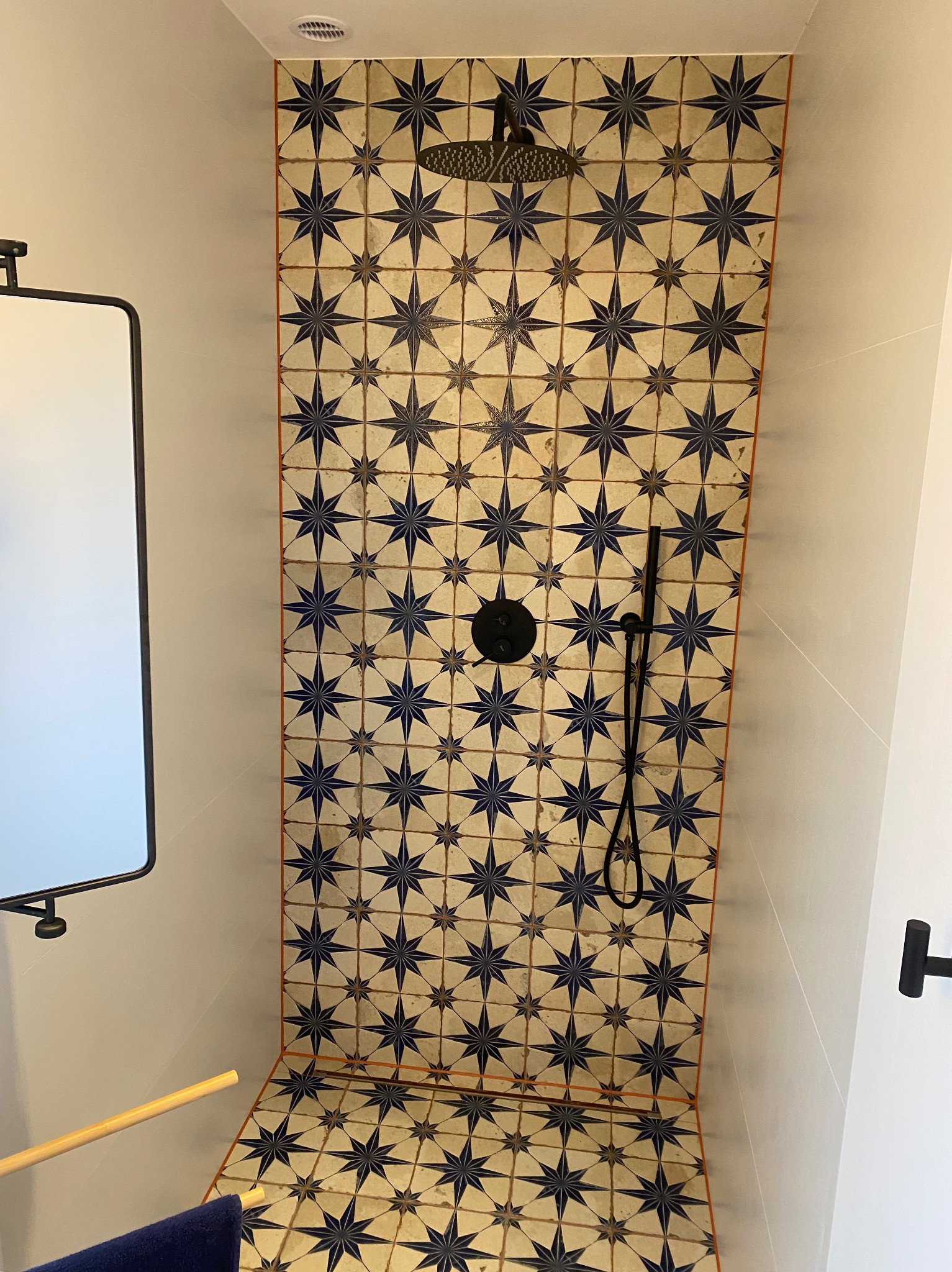Kabina prysznicowa wyłożona dekoracyjnymi, kremowo-granatowymi płytkami w gwiazdy, z czarną armaturą i deszczownicą, widok z dołu.