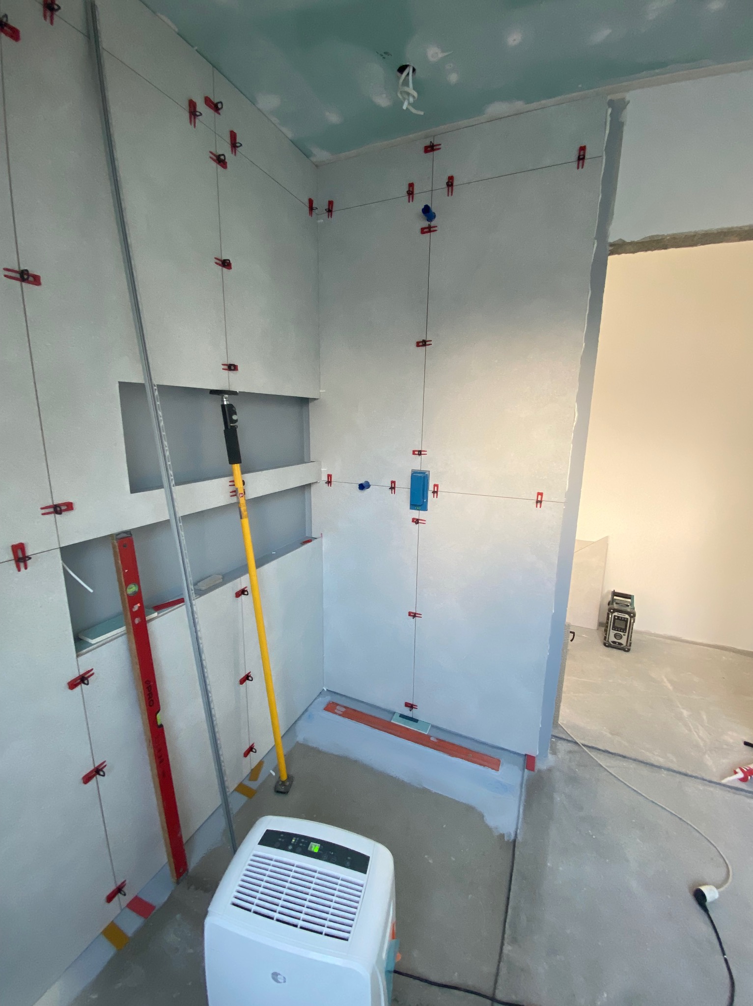 Przygotowanie ścian w łazience do położenia płytek: widoczne profile, poziomice, krzyżyki dystansowe, sznurki wyznaczające linie, oraz osuszacz powietrza.