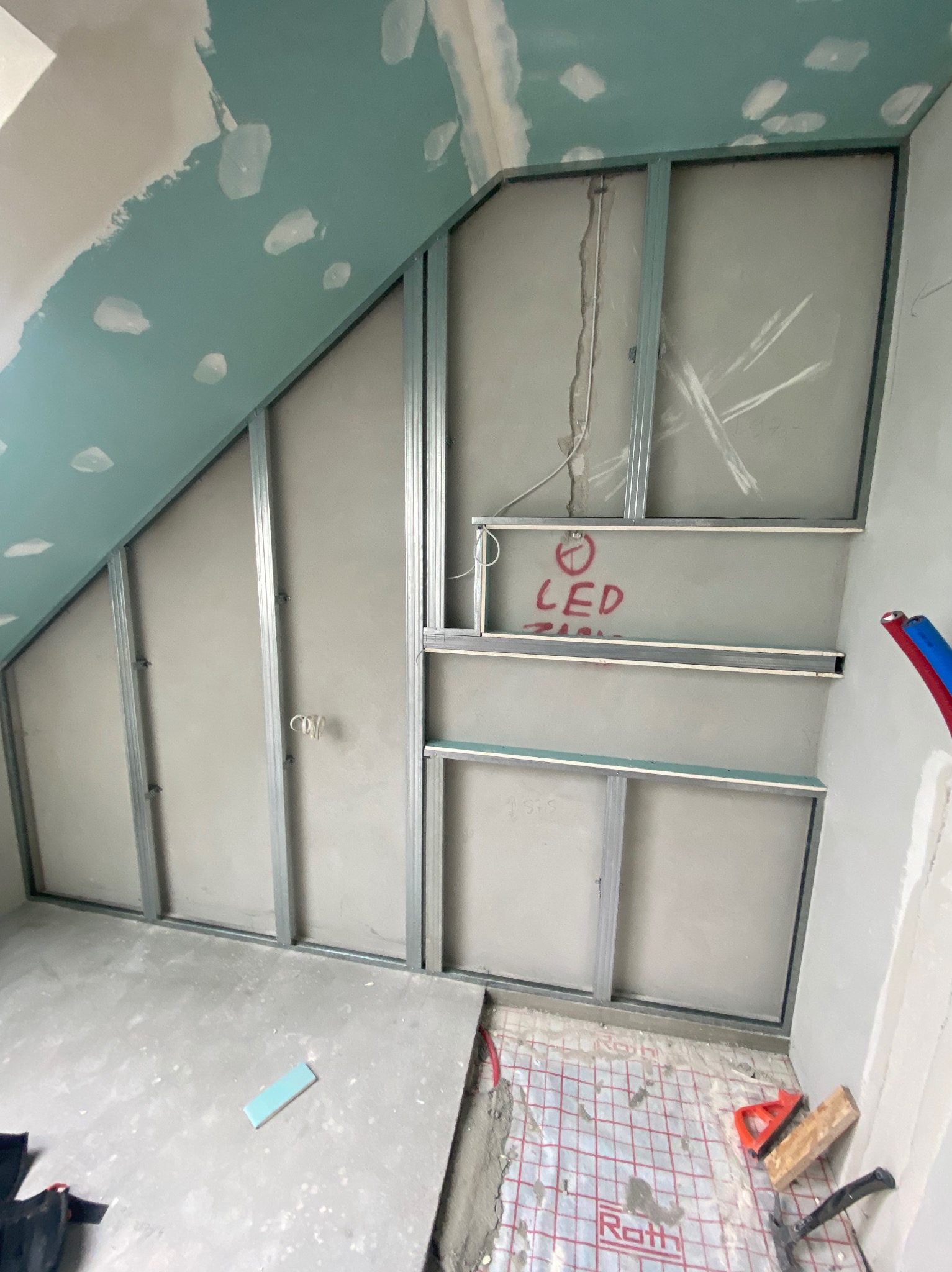 Poddasze w trakcie adaptacji: metalowy stelaż pod zabudowę z płyt karton-gips, widoczne instalacje elektryczne i ogrzewanie podłogowe. Na ścianie napis 'LED'.