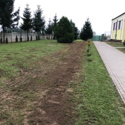 Total Service Usługi Elektryczne - Teren zielony z widocznymi śladami po pracach ziemnych, prawdopodobnie przygotowany pod instalację odgromową, w tle ogrodzenie i budynek z kolorową elewacją.