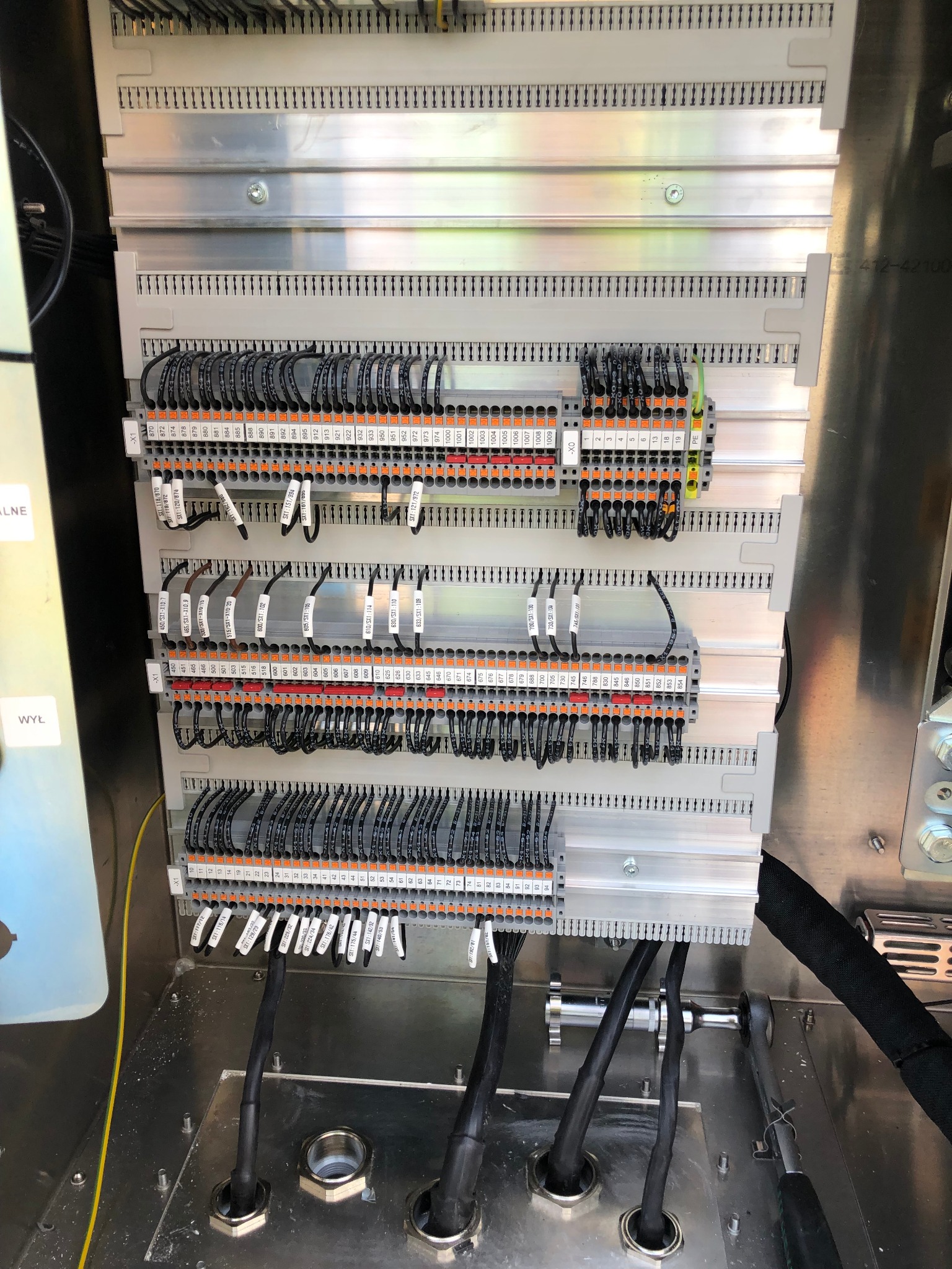 Wnętrze szafy sterowniczej z podłączonymi przewodami elektrycznymi i oznaczeniami w Ostrowcu Świętokrzyskim. Widoczne listwy zaciskowe, kable w peszlach i narzędzia.