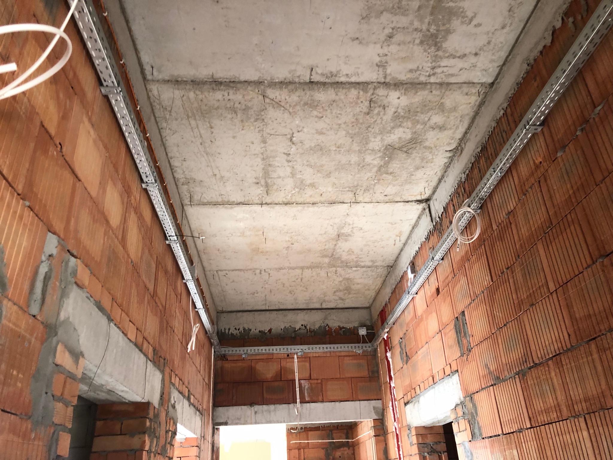 Montaż metalowych korytek kablowych pod sufitem w surowym wnętrzu budynku z ceglanymi ścianami.