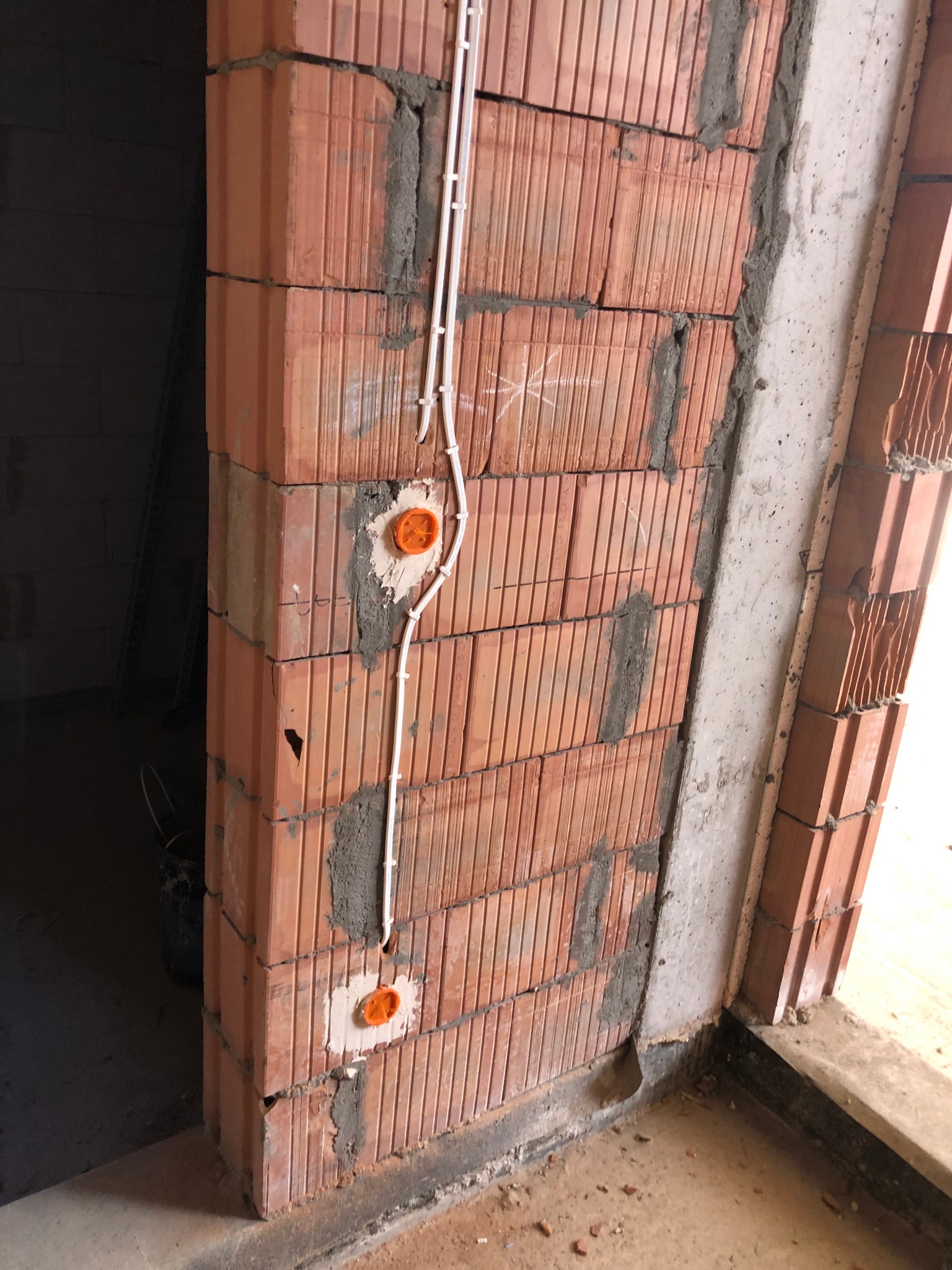 Montaż przewodów elektrycznych w nowo wzniesionej ścianie z cegły ceramicznej, widoczne puszki instalacyjne i przewody w białych rurkach ochronnych.