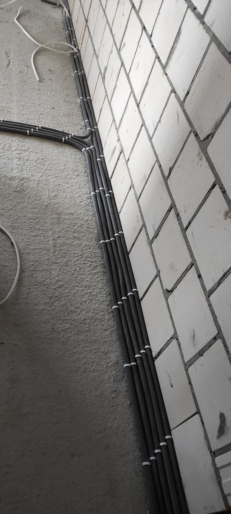 Rury karbowane z przewodami elektrycznymi przymocowane do ściany z białej cegły, instalacja w trakcie wykonywania.