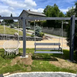 Nowoczesny plac zabaw z huśtawkami na metalowym stelażu, wykończony kostką brukową w odcieniach szarości, na tle zadbanego ogrodu z domem.