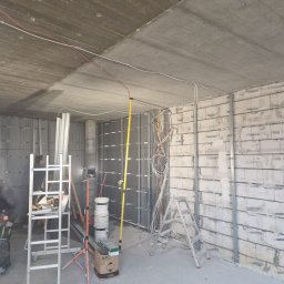 Dzik-Rem - Wnętrze w trakcie prac wykończeniowych: widoczne profile na ścianach, instalacja elektryczna, drabiny i narzędzia. Betonowy sufit z widocznymi przewodami.