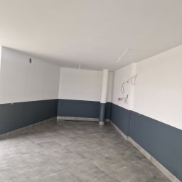 Dzik-Rem - Wnętrze po remoncie: szare płytki podłogowe, ściany pomalowane do połowy na szaro, góra biała. Widoczne wystające kable elektryczne.