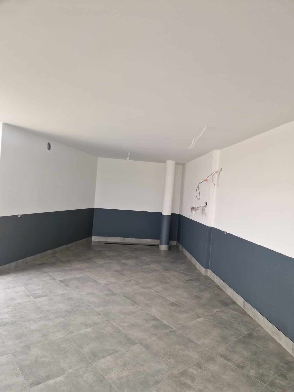 Wnętrze po remoncie: szare płytki podłogowe, ściany pomalowane do połowy na szaro, góra biała. Widoczne wystające kable elektryczne.
