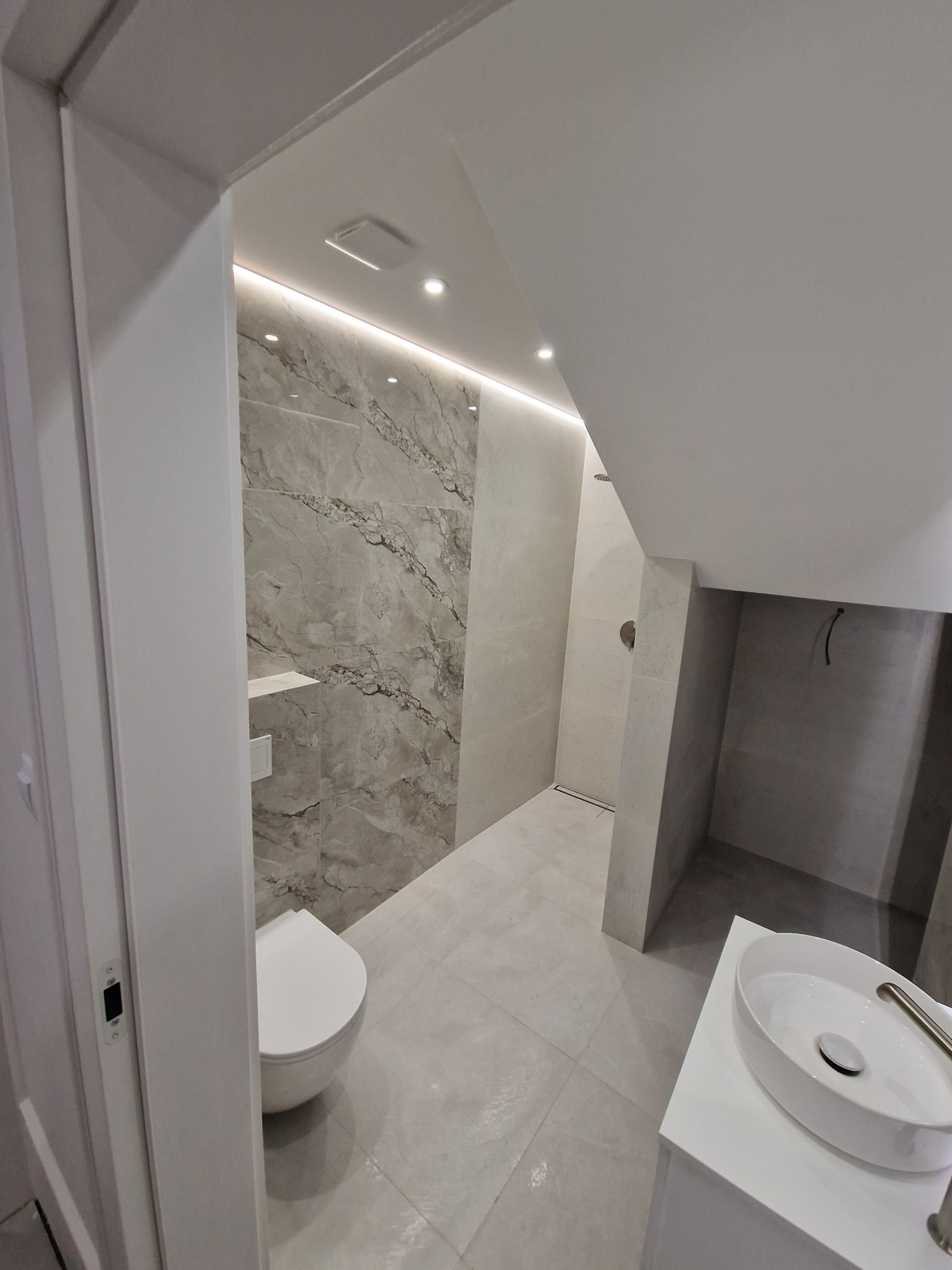 Nowoczesna łazienka w odcieniach szarości i bieli. Uwagę przykuwają marmurowe płytki na ścianie, podświetlenie LED i minimalistyczna umywalka.
