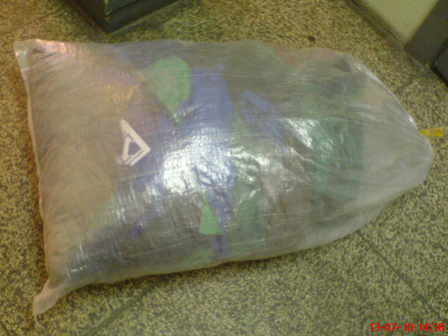 Worek z używaną odzieżą roboczą, widoczne spodnie ogrodniczki z logo, sfotografowany na szarej podłodze.