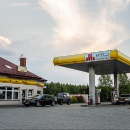 ARCAB Investments Sp. z o.o. - Stacja paliw FP ECO z budynkiem motel-baru w tle, kilka samochodów na brukowanym placu przed dystrybutorami i budynkiem, wieczorne oświetlenie.