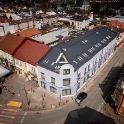 ARCAB Investments Sp. z o.o. - Widok z lotu ptaka na odnowiony budynek mieszkalno-usługowy w centrum miasta z logo 'ARCAB' na elewacji, krzyżujące się ulice, samochody i kościół w tle.