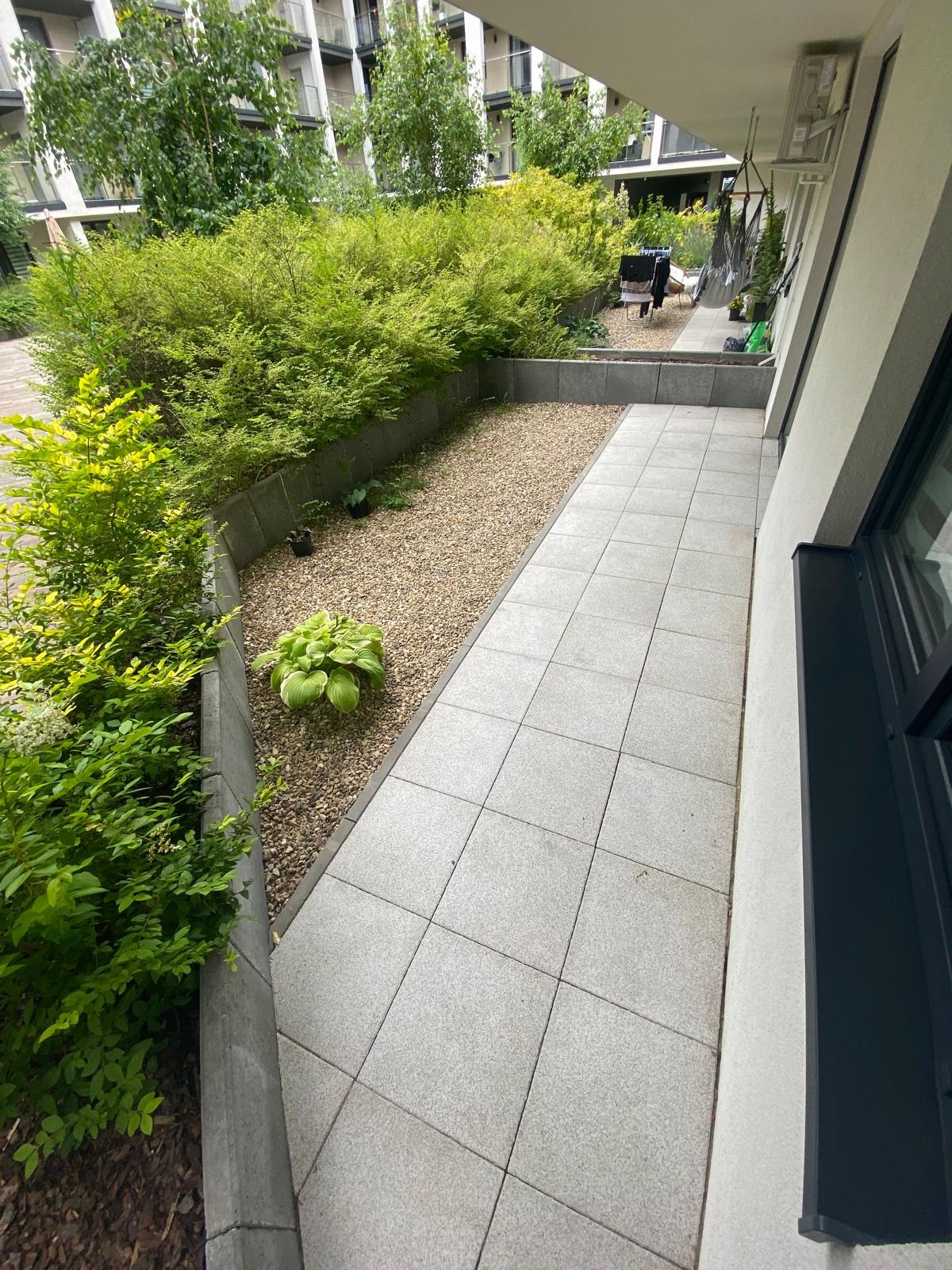 Ułożona z szarych płyt ścieżka na balkonie z wydzielonym obszarem z kamykami i zielenią, widok z góry.