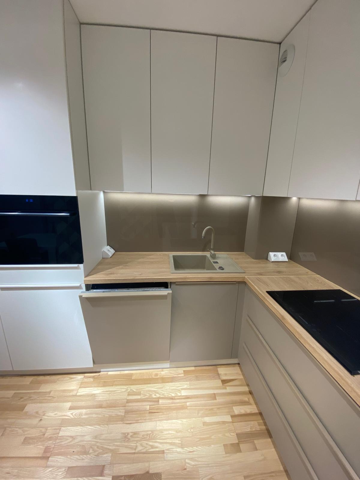 Nowoczesna kuchnia w beżowych odcieniach z drewnianym blatem, zintegrowanym zlewem i płytą indukcyjną, oświetleniem LED pod szafkami wiszącymi i drewnianą podłogą.