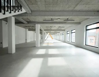 Puste, przestronne wnętrze biurowe z surowym betonowym sufitem, białymi kolumnami i rzędem okien wzdłuż ściany, widok z perspektywy podłogi.