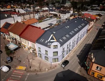 Widok z lotu ptaka na odnowiony budynek mieszkalno-usługowy w centrum miasta z logo 'ARCAB' na elewacji, krzyżujące się ulice, samochody i kościół w tle.