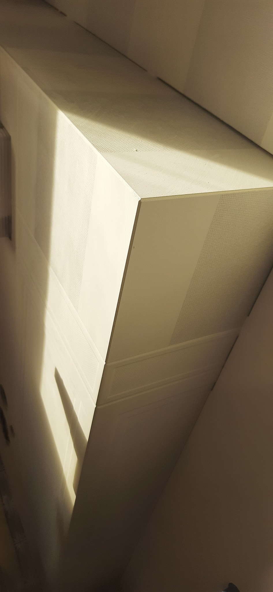 Fragment sufitu podwieszanego z płyt kartonowo-gipsowych, oświetlonego z boku, ukazujący strukturę i łączenia płyt.