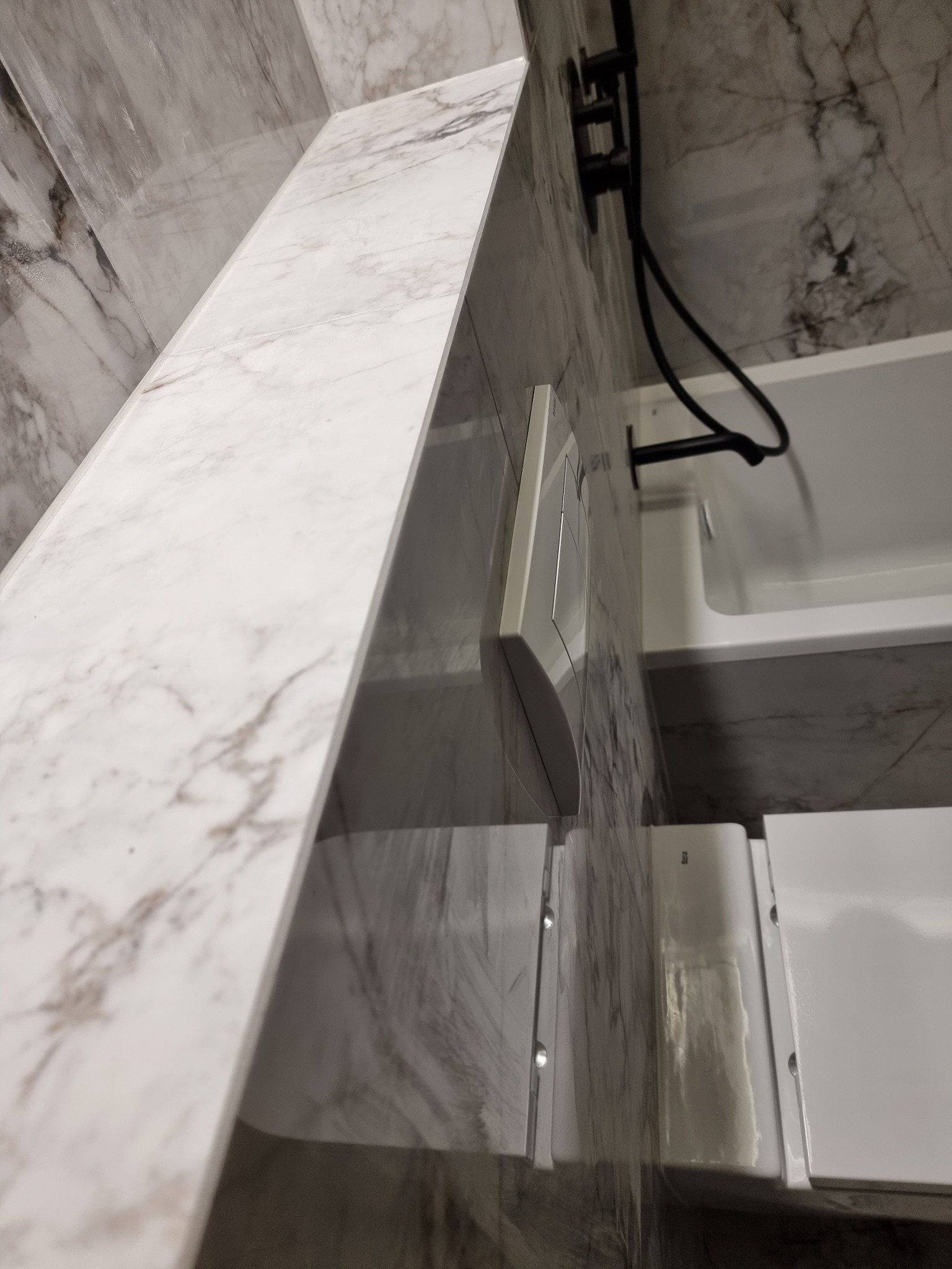 Nowoczesna łazienka z marmurowymi płytkami na ścianach, czarną armaturą i podtynkową spłuczką WC, widok z dołu