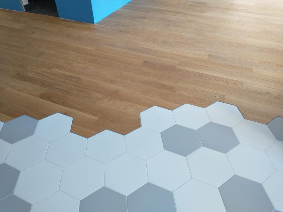 Połączenie podłogi drewnianej z szarymi i białymi płytkami heksagonalnymi, widok na podłogę i fragment niebieskiej ściany.