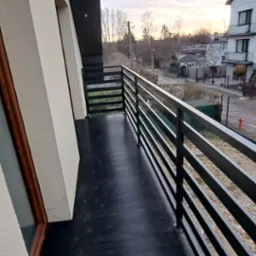 Balkon z prostą, czarną balustradą w Aleksandrowie Łódzkim, widok na ulicę i sąsiednie budynki o zmierzchu.