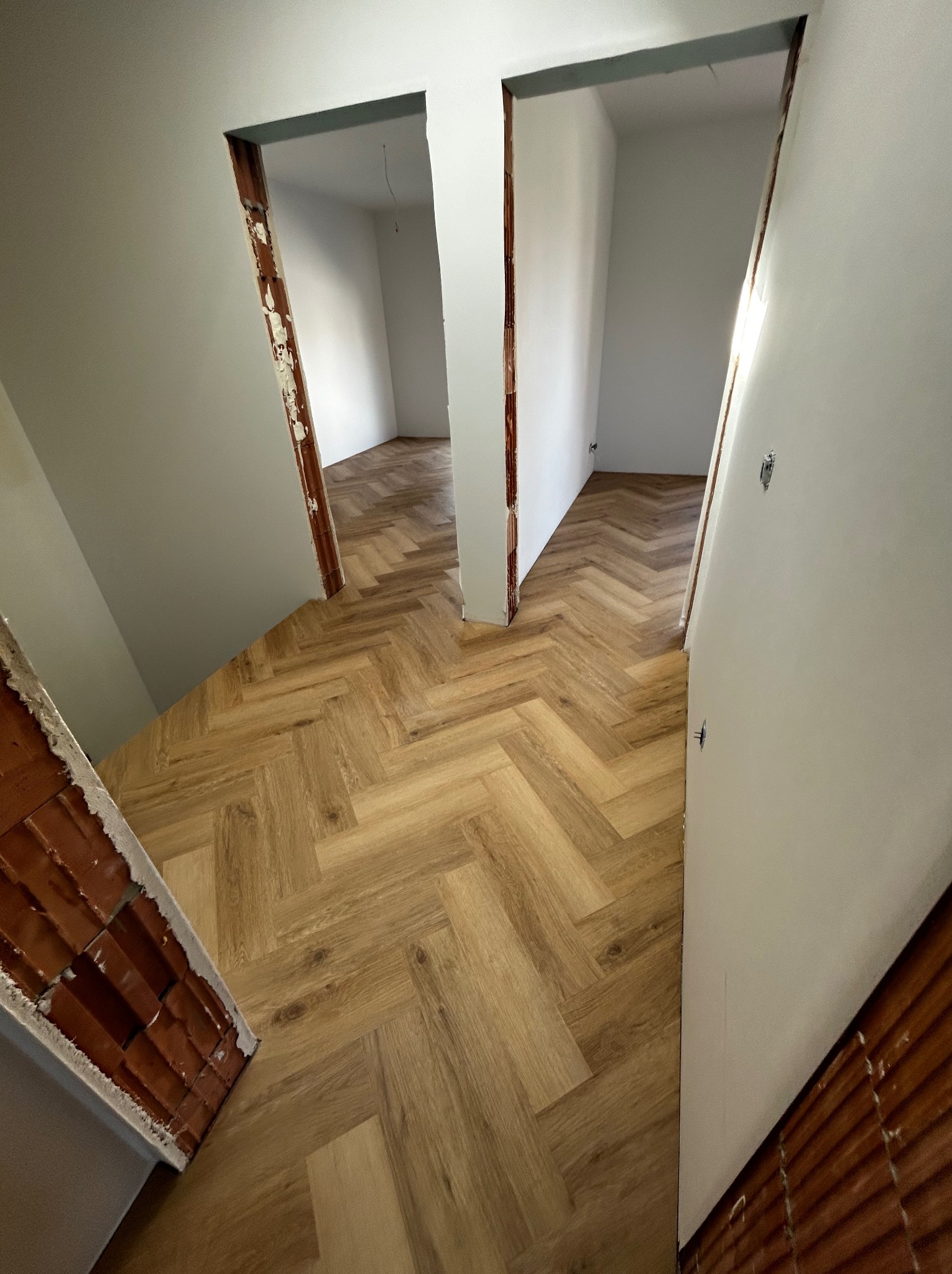 Ułożony parkiet w jodełkę w trakcie remontu, widoczne surowe ościeżnice i przygotowane ściany do malowania.