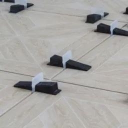 Ułożone płytki podłogowe w jodełkę z systemem poziomowania płytek, jasne spoiny, widok z góry, oświetlenie naturalne.