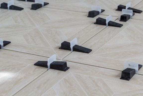 Ułożone płytki podłogowe w jodełkę z systemem poziomowania płytek, jasne spoiny, widok z góry, oświetlenie naturalne.