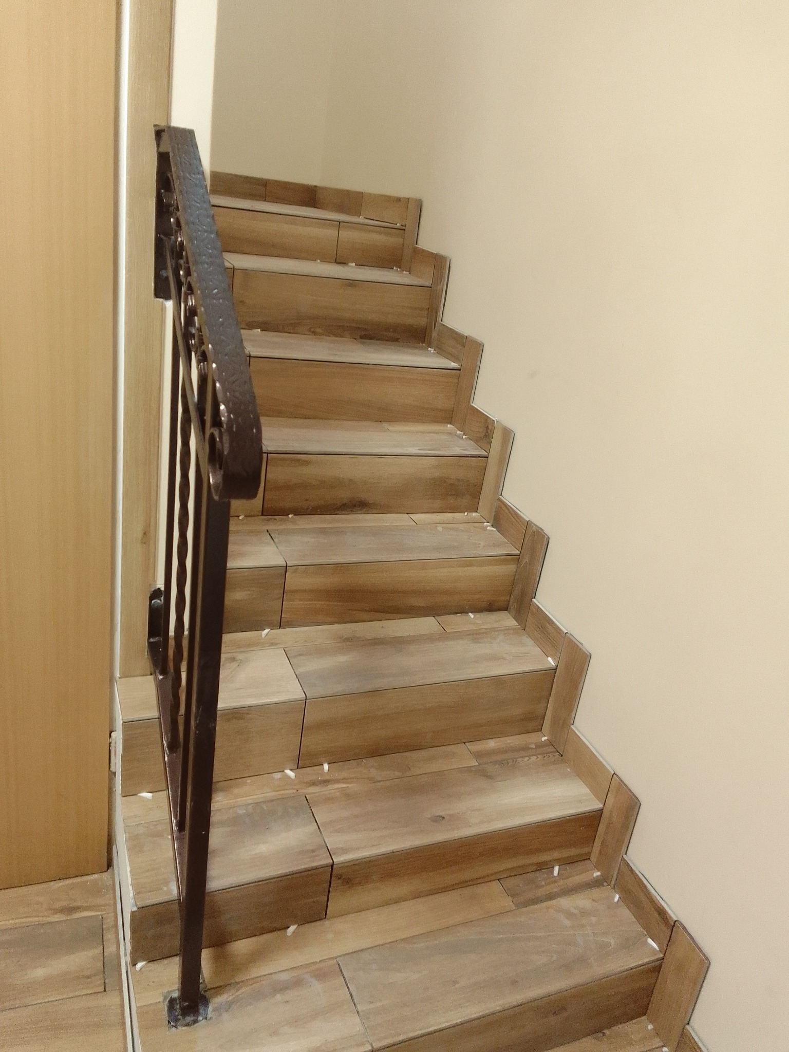 Schody wyłożone płytkami imitującymi drewno, z metalową balustradą, widoczne ślady po kleju i fugowaniu.