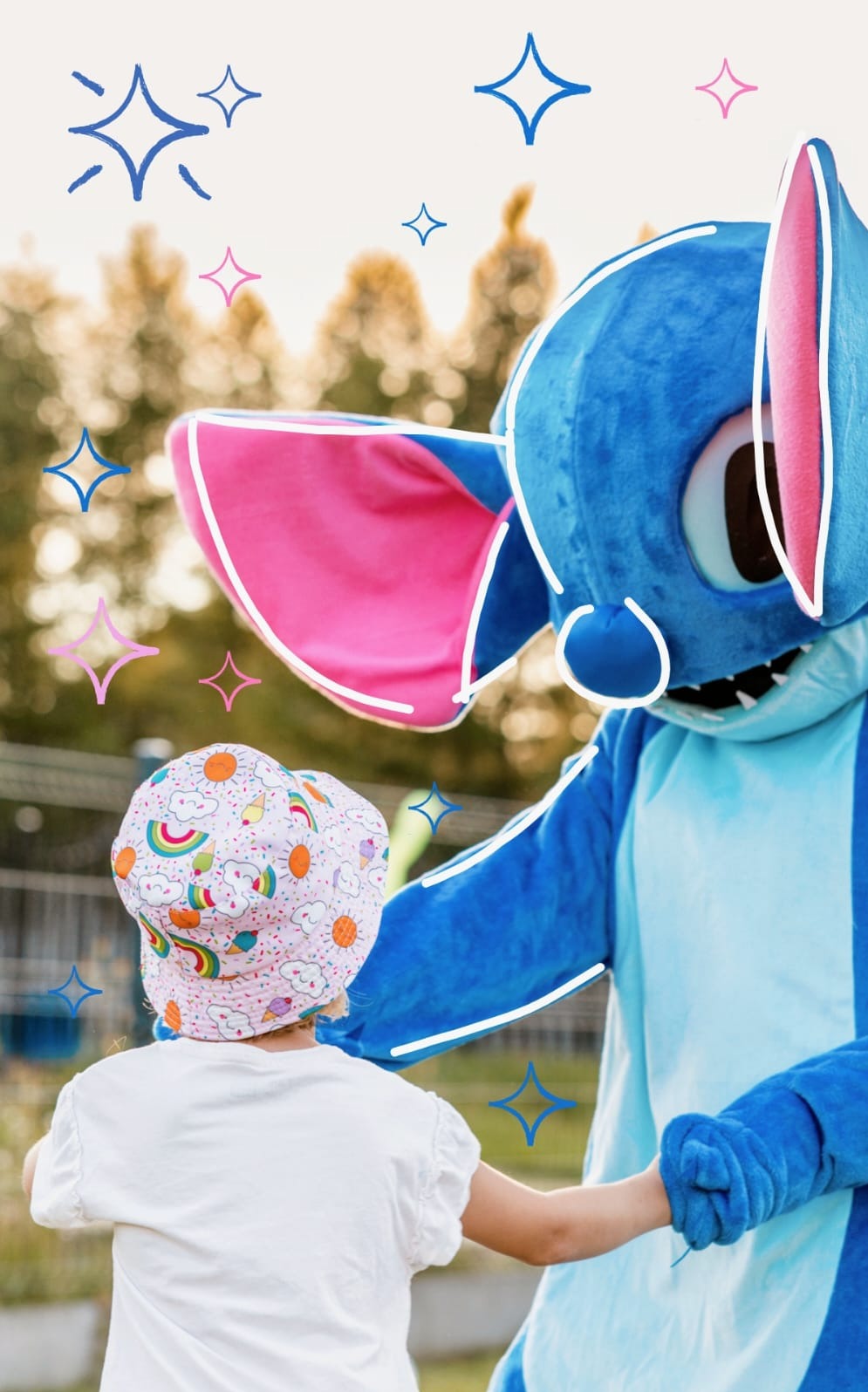 Dziecko trzymające za rękę pluszowego, niebieskiego stwora z różowymi uszami w plenerze, z nakładanymi błyszczącymi gwiazdkami.