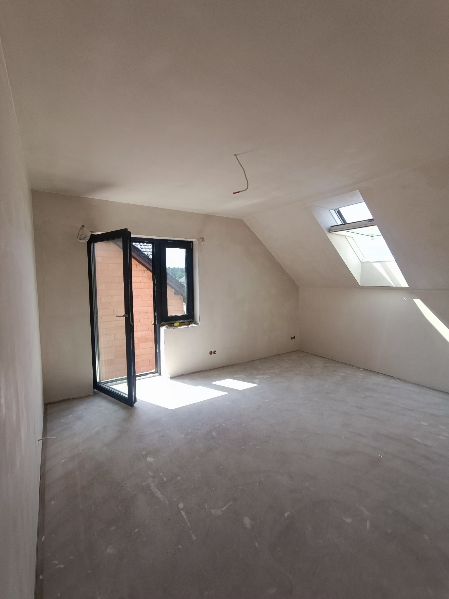 Poddasze po szpachlowaniu ścian i sufitu, widoczne otwarte drzwi balkonowe i okno dachowe, surowa podłoga przed wykończeniem.