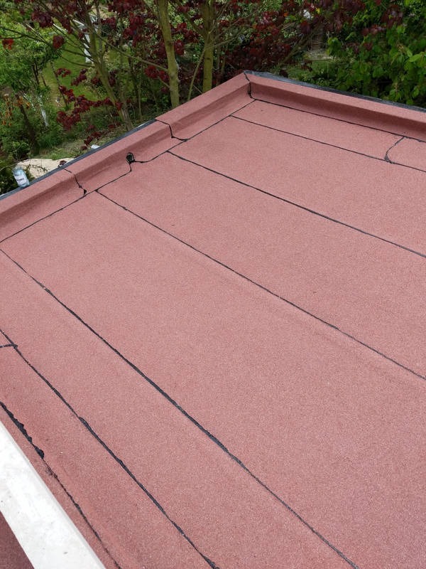 Płaski dach pokryty papą termozgrzewalną, widoczne łączenia i obróbki krawędziowe, drzewa w tle.