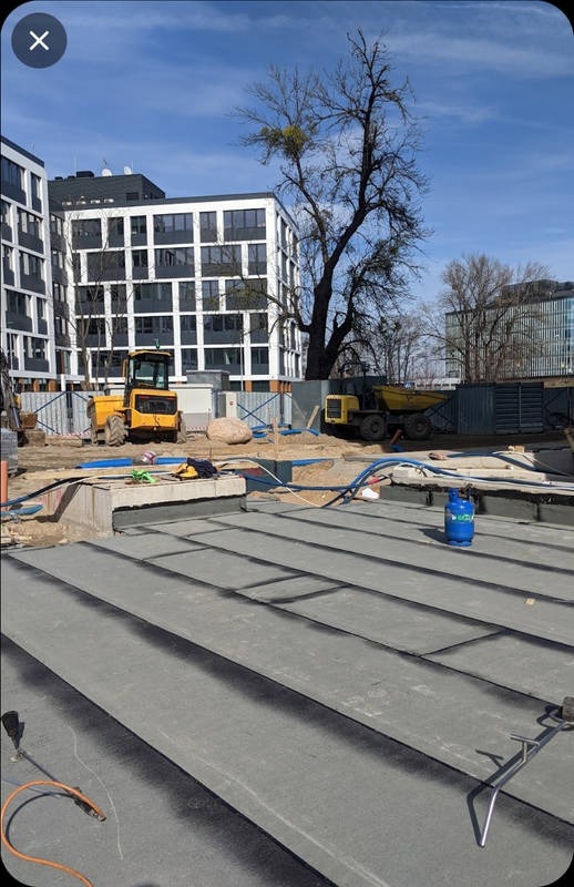 Nowy dach z blachy na budynku wielorodzinnym w trakcie budowy, widoczne maszyny budowlane i butla gazowa.