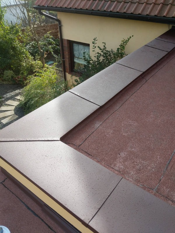 Nowa obróbka blacharska dachu z widocznymi kroplami wody, wykonana na tle ogrodu z kamienną ścieżką.