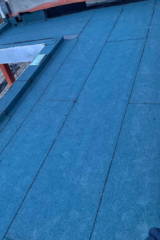 Niebieskie pokrycie dachowe z papy bitumicznej na płaskim dachu, widoczne łączenia i fragment konstrukcji dachu.