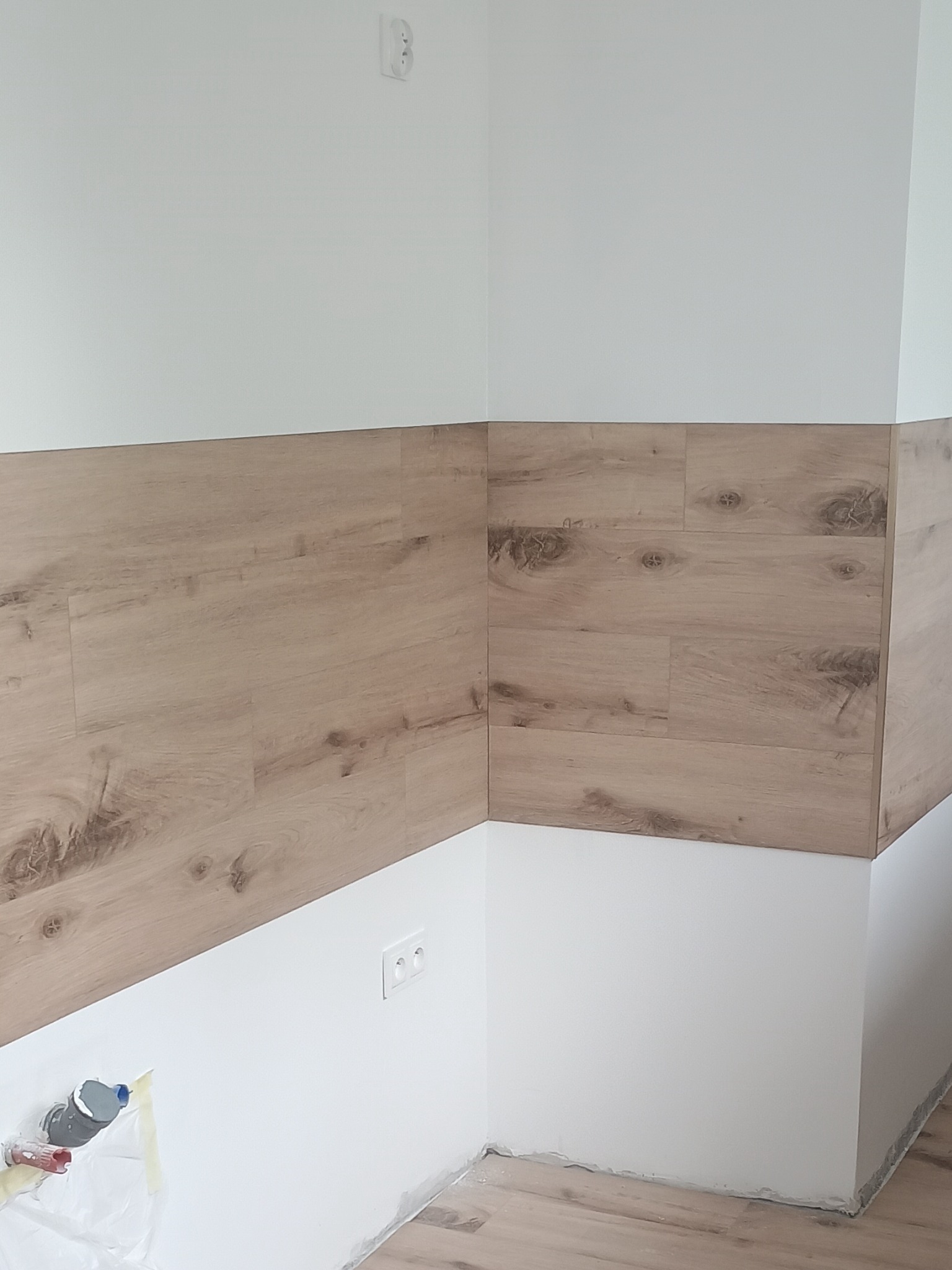 Fragment wnętrza po montażu paneli ściennych imitujących drewno, z widocznymi gniazdkami elektrycznymi i elementami instalacji wodnej w dolnej części ściany.