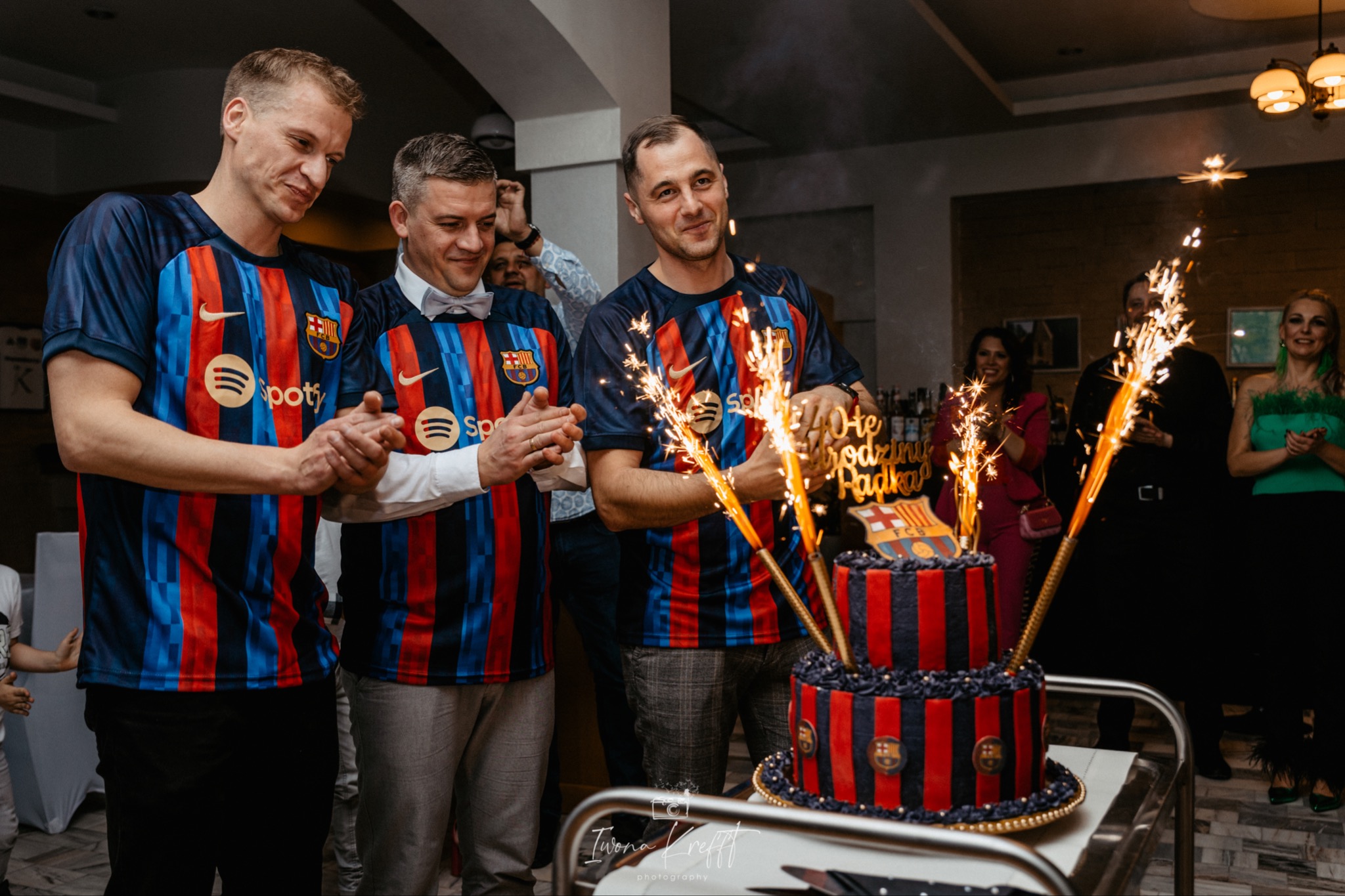 Trzej mężczyźni w koszulkach FC Barcelona świętują urodziny z tortem i fontannami iskier.