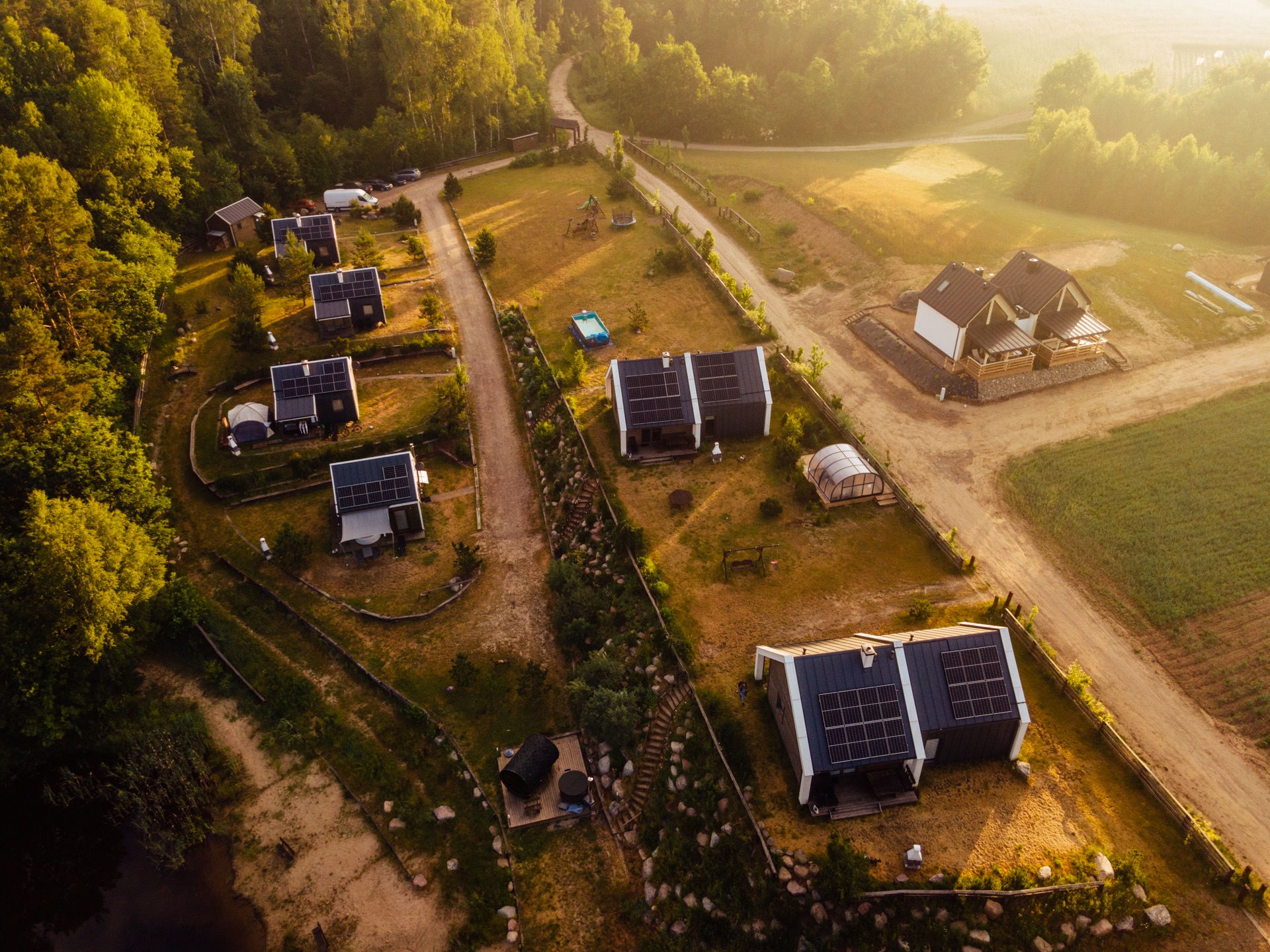 Widok z lotu ptaka na osiedle domków letniskowych z panelami słonecznymi, otoczonych lasem w promieniach wschodzącego słońca.