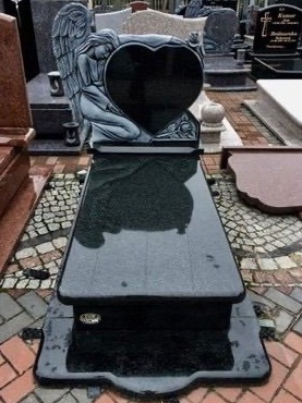 Czarny nagrobek z wyrytym aniołem i sercem, ustawiony na wzorzystej kostce brukowej, widok z góry.